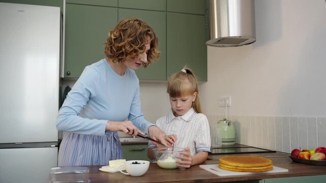 Mother and daughter bake layered cake together in cozy sunlit kitchen, 25 fps