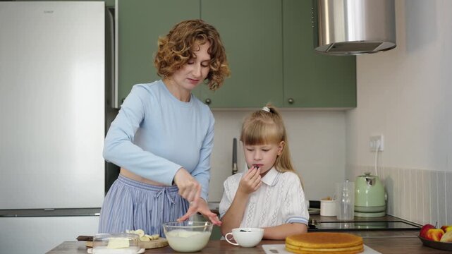 Mother and daughter bake layered cake together in cozy sunlit kitchen, 25 fps