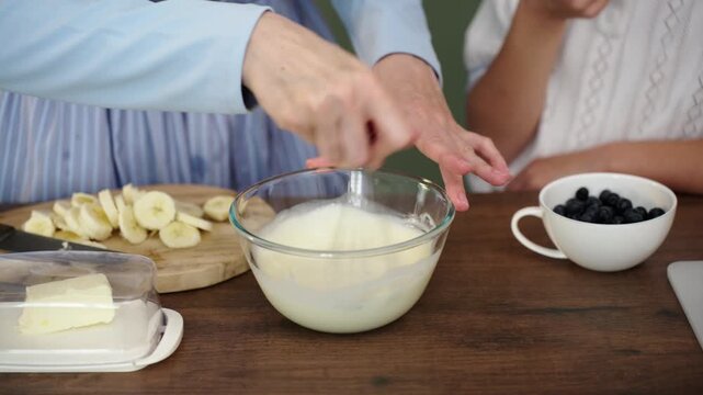 Mother and daughter bake layered cake together in cozy sunlit kitchen, 25 fps