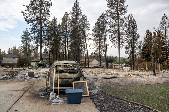 Spokane, Washington, United States - 14 August 2026: View of a burned vehicle and debris outside a destroyed home, with sifting tools and insurance flyers left for homeowners.
