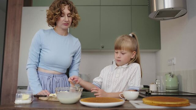 Mother and daughter bake layered cake together in cozy sunlit kitchen, 25 fps