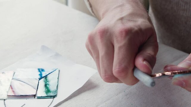 Copper tape is molded onto a piece of cut glass using the back of a marker during an art class.