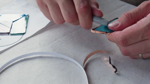 Art student molds a piece of copper tape onto a recently cut piece of stained glass that they will use to make a small piece during art class.