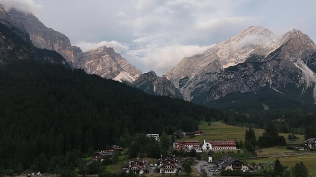 serene alpine valley with snow-capped mountains and village houses in the foreground. aerial view, looking down at the picturesque landscape with green fields and rocky terrain.