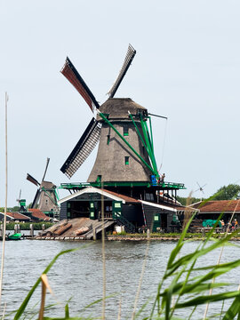Zaandam, Netherlands - 31 July 2026: View of a traditional Dutch windmill with green wooden structures and a thatched roof situated by the water.