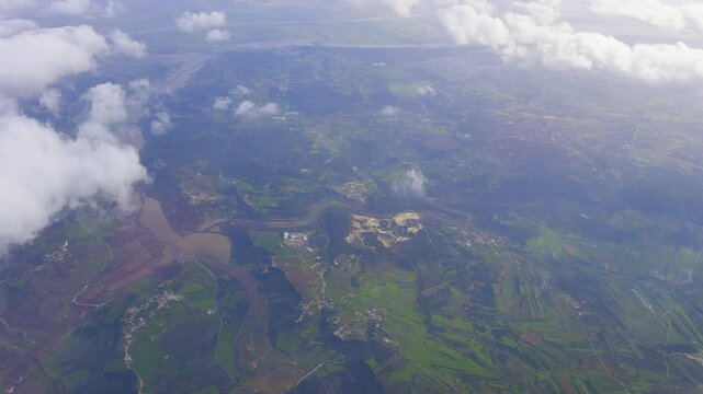 Scenic aerial view from an airplane window showing a winding river, green fields, and scattered villages beneath soft clouds.