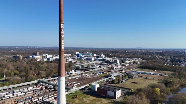 Drone circles the Bayer tower from the riverside while revealing storage areas and the wider chemical plant complex.