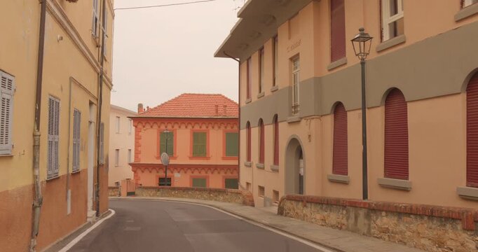 Quiet curved street runs between pastel residential buildings with shutters and a lamppost in Imperia old town, Porto Maurizio, Italian Riviera, Italy