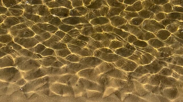 Sunlit ripples shimmer across clear shallow coastal water. High quality 4k footage