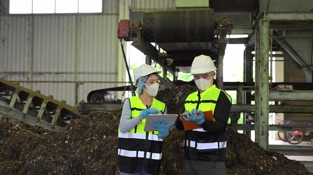 Asian environmental engineers in safety PPE inspect organic compost and biomass processing at a recycling plant