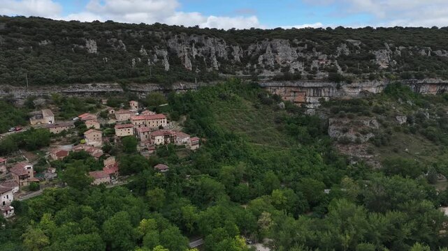 serene canyon landscape with rock formations and lush vegetation under a cloudy sky. aerial perspective of natural outdoor environment. Risco los camellos, Cascada de Orbaneja del Castillo
