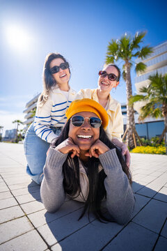 Vertical. Three female friends enjoy a playful pose outdoors in a bright modern neighborhood, creating a fun lifestyle portrait with friendship and sunny travel vibes.
