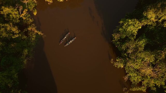 Aerial drone shot of two canoes paddling on a river through the lush amazonian rainforest
