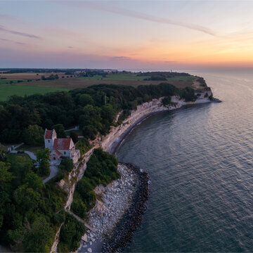 Aerial view of the historic Hojerup old church perched on the edge of the white chalk cliffs overlooking the sea at sunset in Hojerup, Denmark.