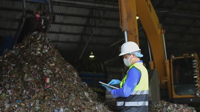 Engineer in safety gear using a digital tablet to supervise industrial waste sorting and plastic recycling