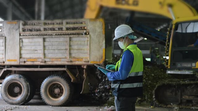 Engineer in safety gear using a digital tablet to supervise industrial waste sorting and plastic recycling