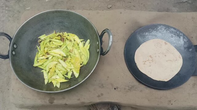 Traditional cooking of roti on tawa and vegetable in kadhai on a clay stove or chulha in a rural kitchen. Homemade food preparation showing village lifestyle and traditional Indian cooking methods.