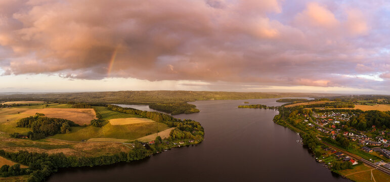 Aerial view of Himmelbjerget hill overlooking Julso lake with lush fields, rolling hills, and a rainbow under a dramatic cloudy sky in Skanderborg, Skanderborg Municipality, Denmark.