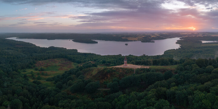 Aerial view of Himmelbjerget tower overlooking the lush forests and the serene Julso lake during a vibrant sunset in Skanderborg Municipality, Skanderborg Municipal, Denmark.