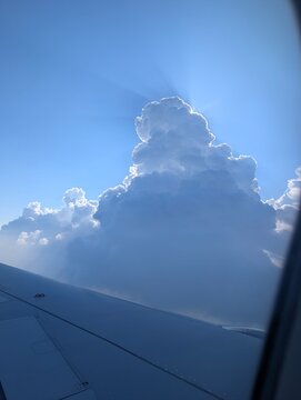 Spectacular aerial view from an airplane window, showing sun rays piercing through a massive cumulus cloud formation under a clear blue sky. Flight Osaka-Seoul.