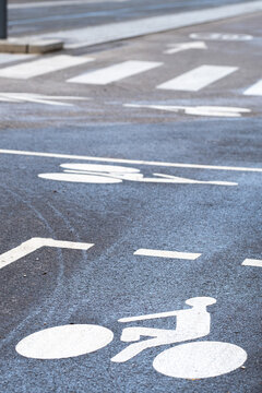 Empty wet bike lane in Lyon with bicycle symbol and road marking leading toward a pedestrian crossing through urban cycling infrastructure after rain