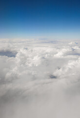 Fototapeta premium Clouds floating high in the clear blue sky, creating a serene and vast atmospheric view from an airplane window
