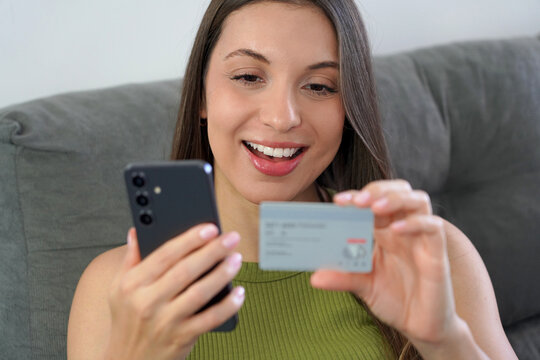 Close up of happy Brazilian woman reading credit card number during online shopping with mobile phone