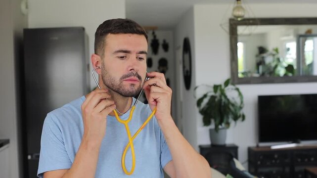Man putting on a stethoscope at home to listen to his own heart with an anxious expression