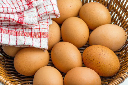 Wicker basket full of brown eggs next to folded kitchen towel isolated on white