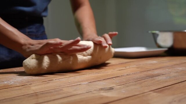 Close-up of hands kneading bread dough on a wooden table in a home kitchen, showing baking, cooking, and handmade food preparation with a warm rustic feel.