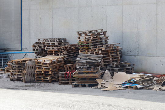 Storage area for wooden pallets, cardboard, and paper next to a warehouse. Wood and paper waste collected for recycling.