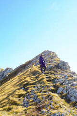 Female traveler walking down steep golden grass mountain ridge in Durmitor National Park. Highlights solo adventure, nature-based wellbeing, and off-season high-altitude exploration in Montenegro. © tanyatorgonskaya