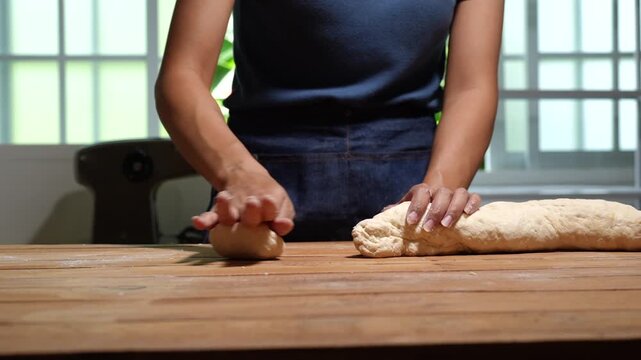Woman shaping and kneading fresh dough on a wooden table in a bright kitchen, showing home baking, cooking skills, and handmade bread preparation.