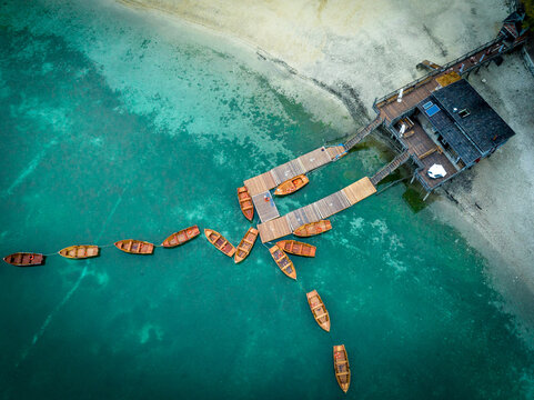 02 October 2022: View of wooden boats moored at a pier on a clear turquoise lake with a sandy shoreline.