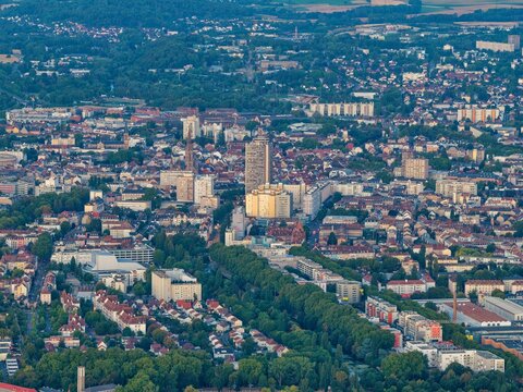 Aerial view of the city of Mulhouse featuring the Tour de l'Europe, historic cathedral spire, dense residential rooftops, and lush green urban parks in Mulhouse, Grand Est, France.