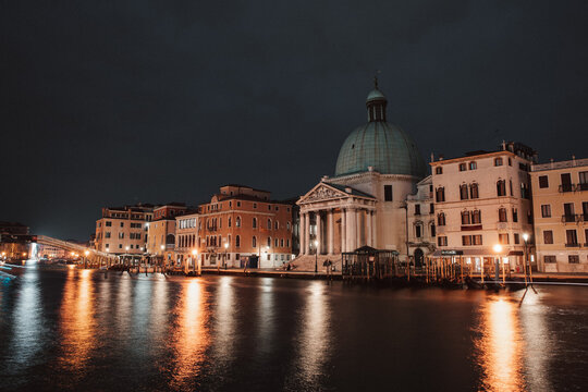 Venice, Italy - 05 October 2022: View of the San Simeone Piccolo church illuminated at night along the Grand Canal with historic buildings and reflections on the water.