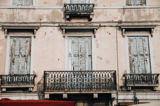 04 October 2022: View of a historic building facade featuring weathered wooden shutters, ornate wrought iron balconies, and textured plaster walls.