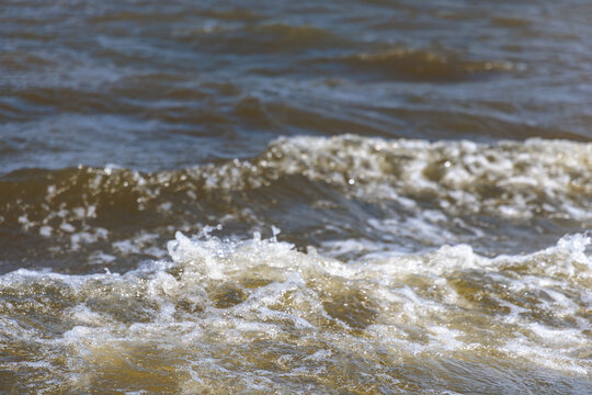 Close up of muddy water waves with white foam splashing on river surface, water pollution and natural energy concept