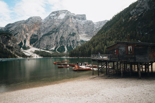 Braies, Italy - 02 October 2022: View of the wooden boathouse on stilts at Lago di Braies with rowing boats moored at the dock and the dramatic Dolomite mountains in the background.
