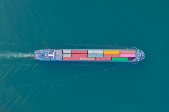 Aerial view of a cargo ship carrying colorful shipping containers across the calm blue water in Bantzenheim, Grand Est, France.