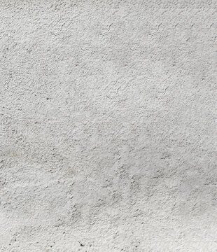 Full frame light grey rough stucco wall background featuring a dense pebbled surface, granular plaster texture, and subtle uneven patches, ideal for raw architectural design overlays.