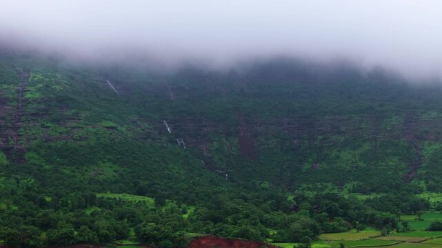 Scenic Aerial View of the Sahyadri Mountains Covered in Floating Clouds with Small Waterfalls Cascading Down Lush Green Slopes, Monsoon Landscape, Misty Hills, Dense Forest and Breathtaking Western Gh