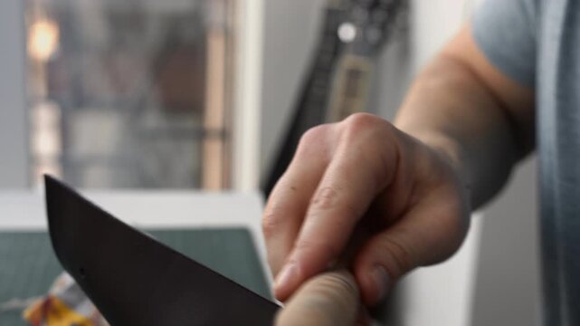 Close-up of a craftsman's hands using a wooden slicker to polish and finish the raw edge of a handmade dark leather accessory