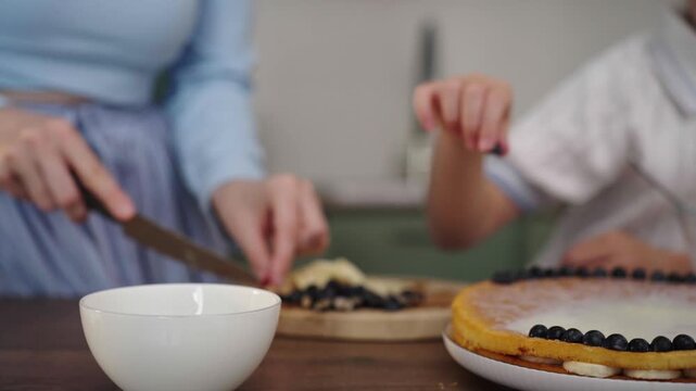 Mother and daughter bake layered cake together in cozy sunlit kitchen, 25 fps