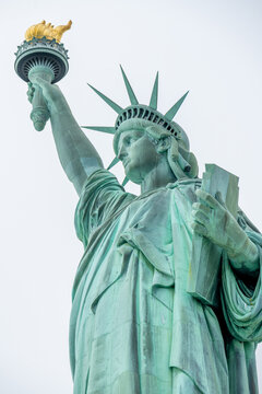 New York, United States - 16 April 2023: View of the Statue of Liberty holding her torch high against a bright sky, showcasing the iconic copper statue's intricate details.