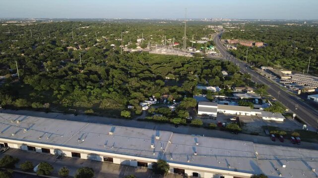 Logistics warehouse rooftops, utility substations line Evers Road across Northwest Bexar County. Industrial storage properties border lush green woodland canopies in San Antonio, Texas