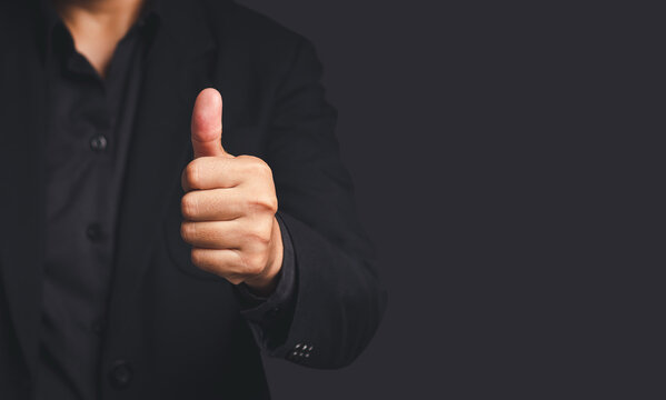 Person Giving Thumbs Up Gesture on Dark Background