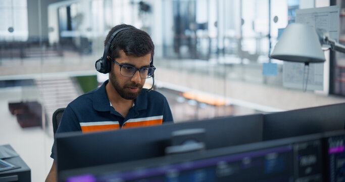 Concentrated Indian Male Software Developer in Glasses and Headset Writing Program Code on Dual Computer Screens, Building Applications and Assisting Clients Online With a Diverse Team in an Office.