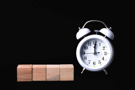 Blank wooden blocks and white analog alarm clock on black background