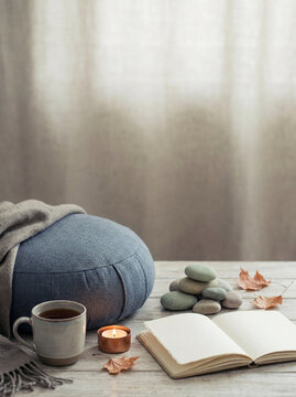 Cozy Zen Meditation and Mindfulness Corner with Blue Zafu Cushion, Open Journal, Hot Tea, Lit Candle, and Balanced Stones for Relaxation, Postcard Background with Copy Space